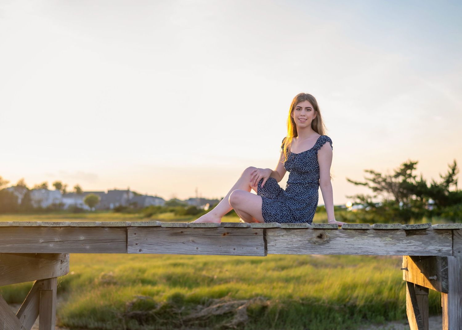 Scenic outdoor portrait session at golden hour with wooden fence and coastal vegetation.