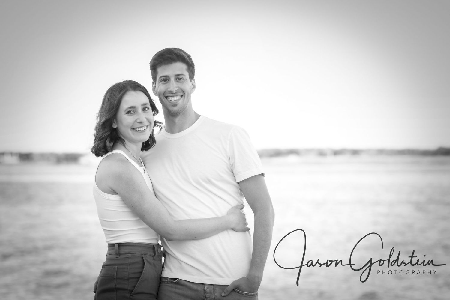 Black and white portrait of a couple in casual attire against a soft gradient background.