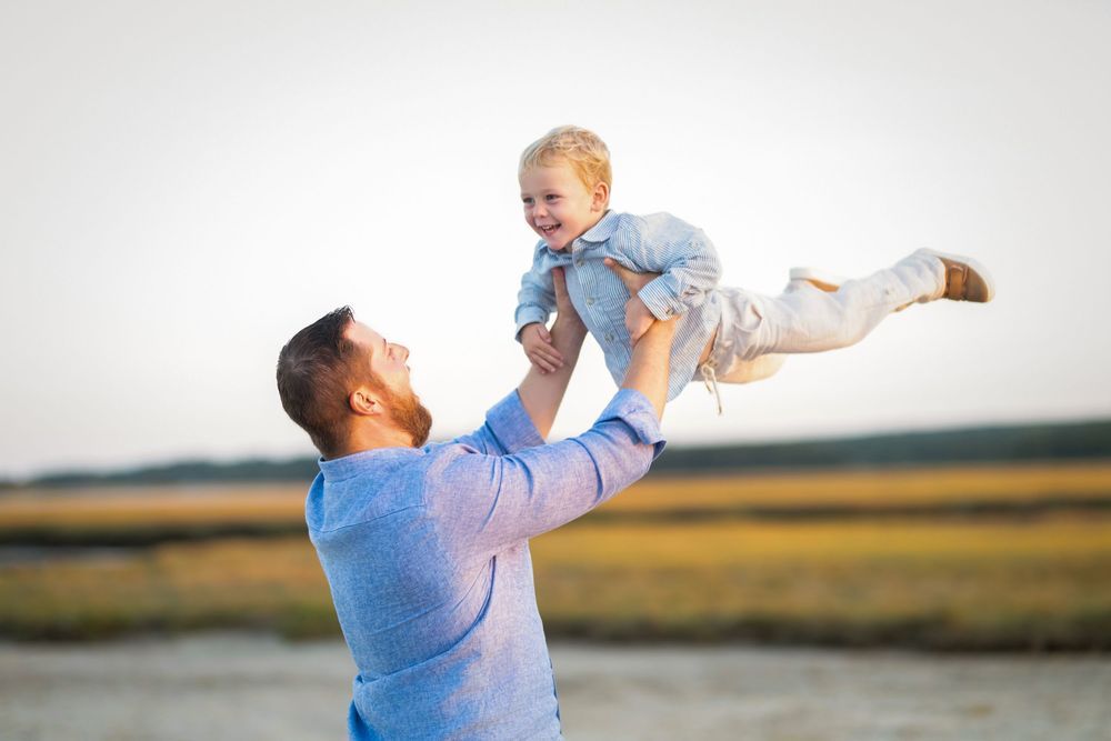 A joyful moment between parent and child playing together outdoors at sunset near a waterfront.