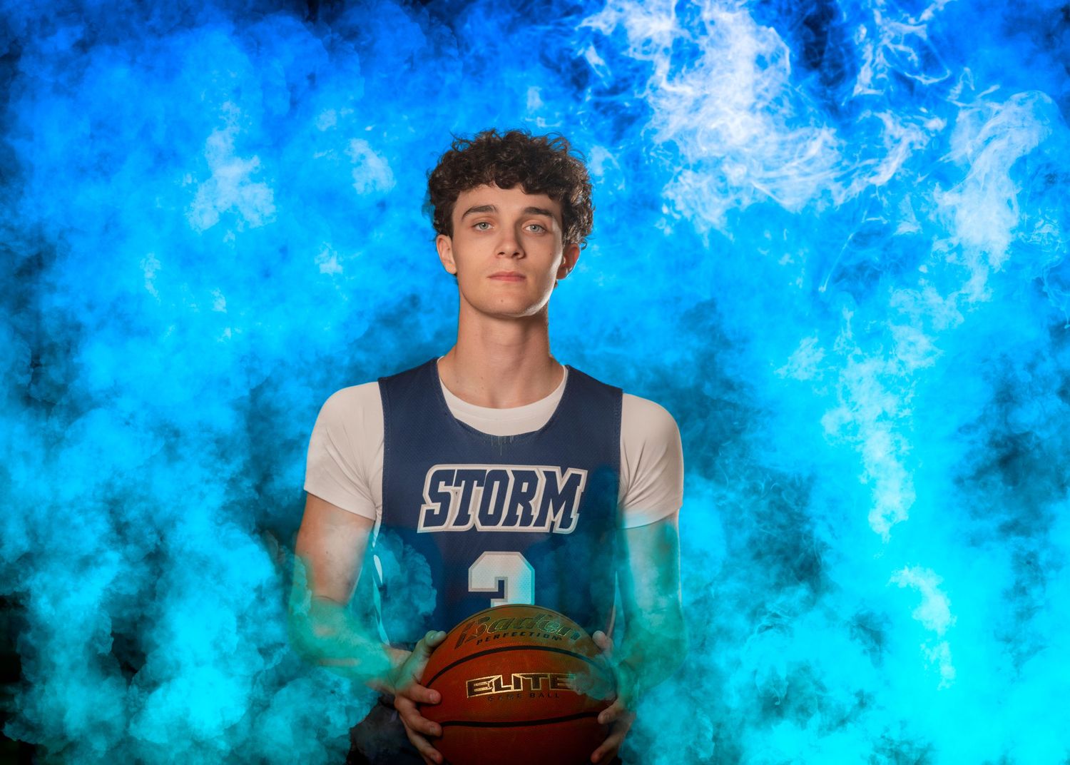 Teen basketball player in Storm jersey holding ball posed against dramatic blue smoke background.
