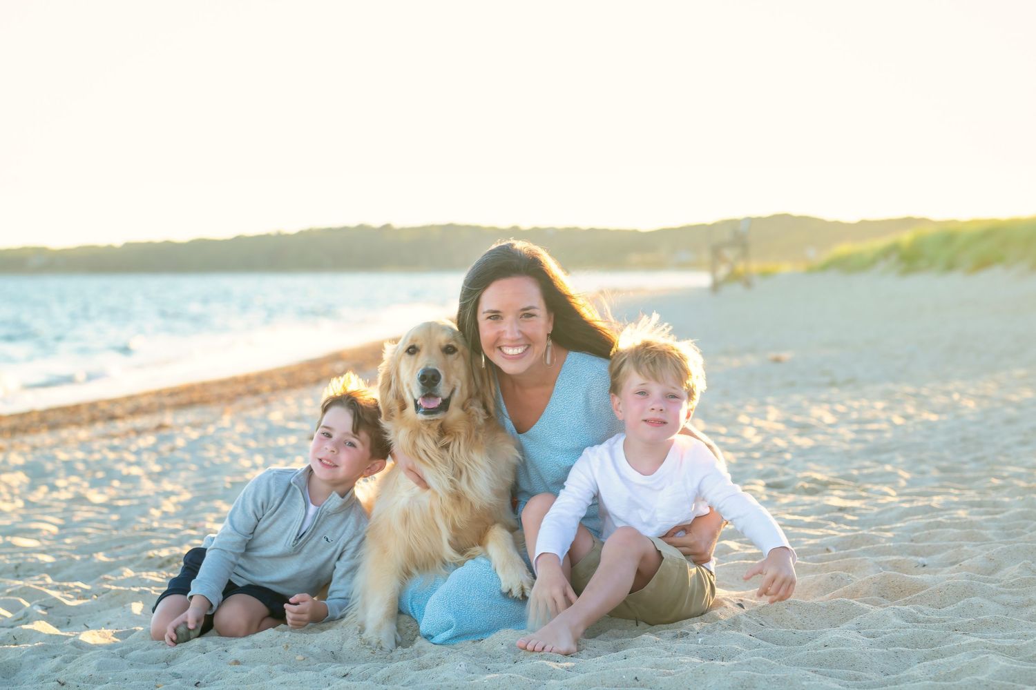 A happy family with their golden retriever sitting together on a sunny beach at sunset.