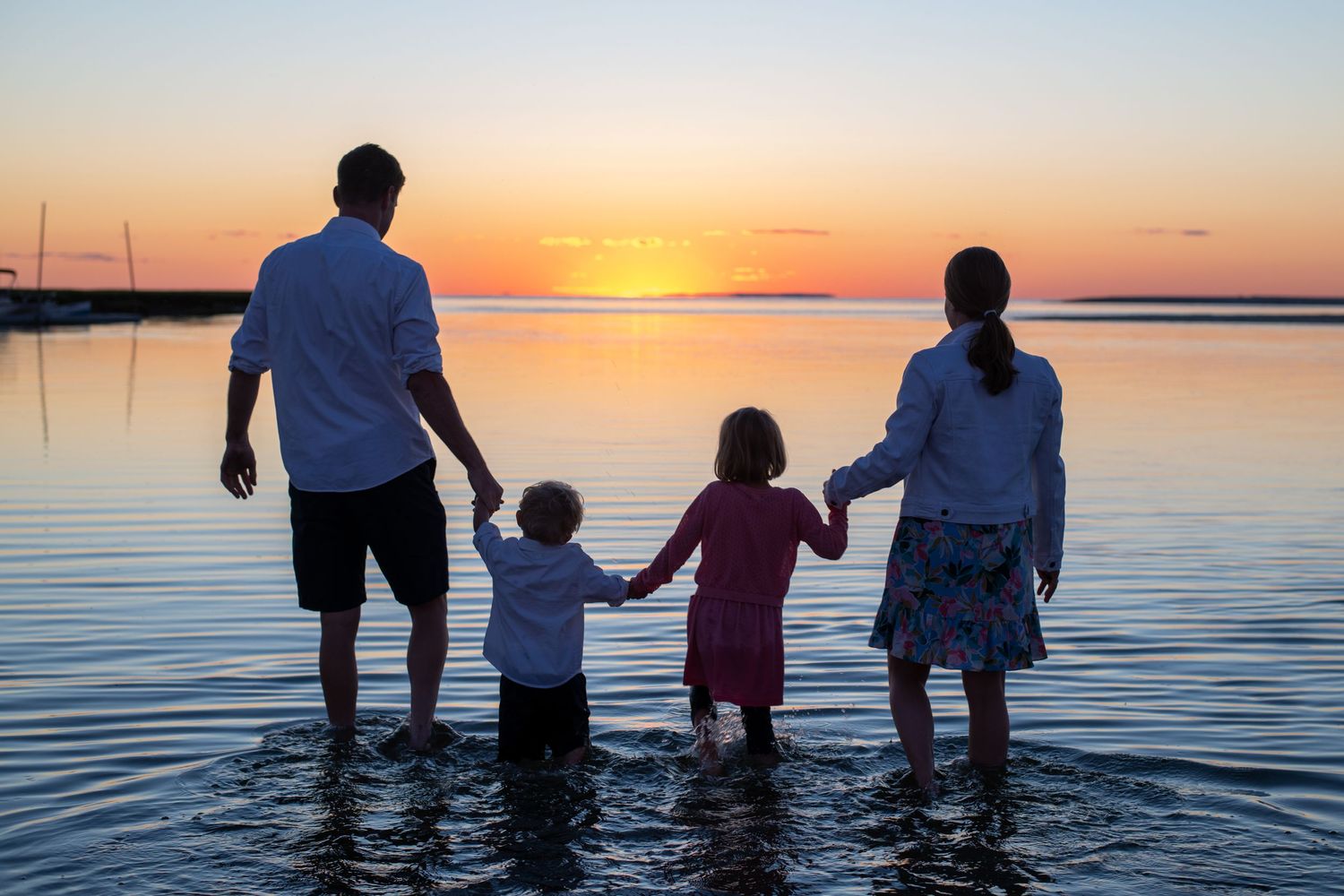 Silhouettes of people standing in calm water against a vibrant orange sunset sky.