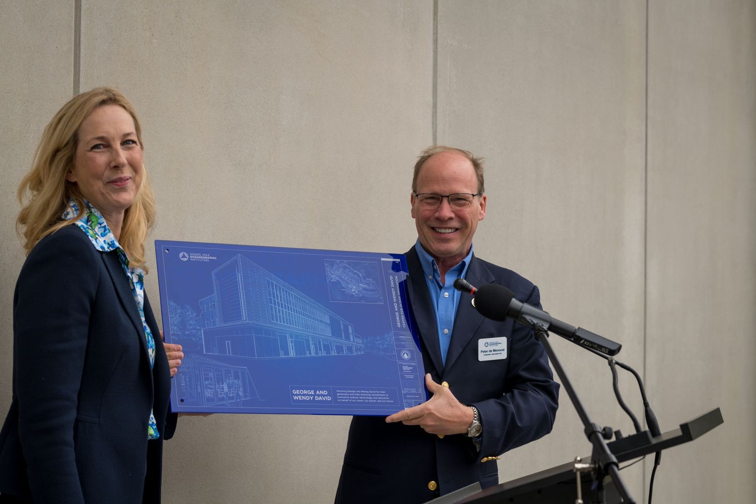 Two presenters holding a large blueprint diagram during a presentation at an ocean innovation center.