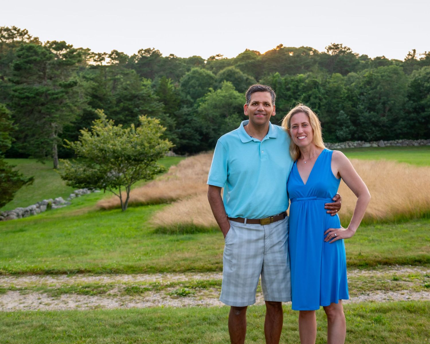 Outdoor summer portrait session in a grassy field with trees in background.