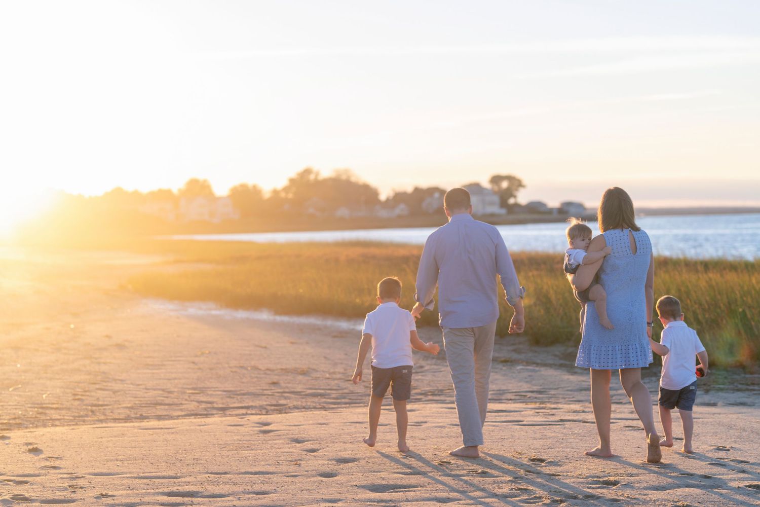 Family walking together on a beach at sunset with silhouettes against the orange sky.