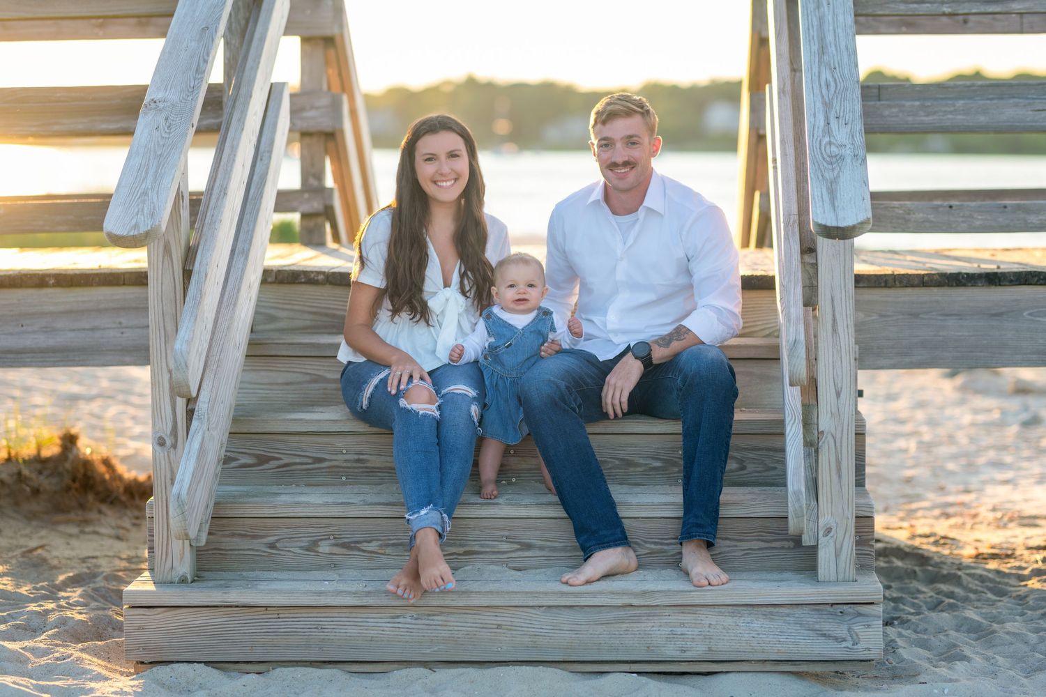 Family sitting together on wooden pier during sunset at beach.