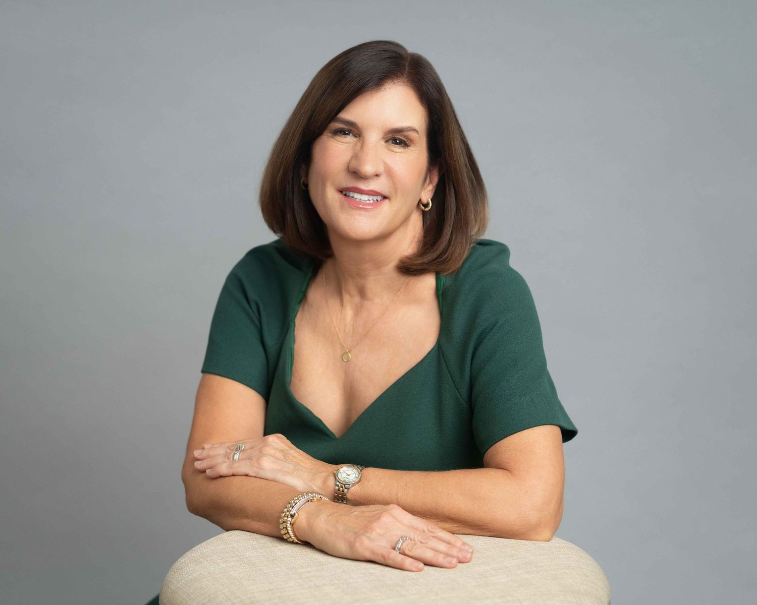 Professional woman in green top smiling, seated with arms crossed, wearing a watch and bracelet.