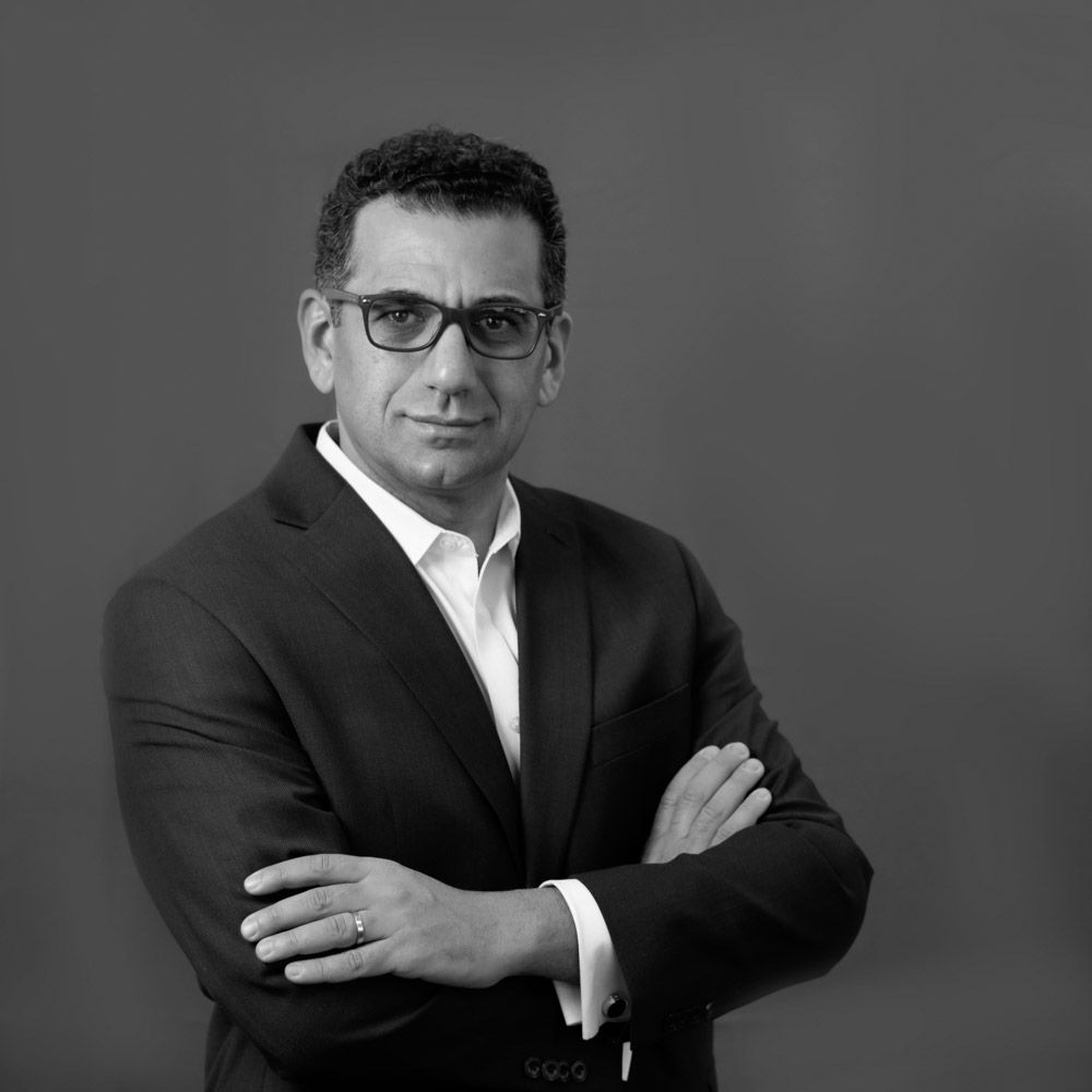 Professional man in suit with crossed arms, wearing glasses, black and white portrait photo.