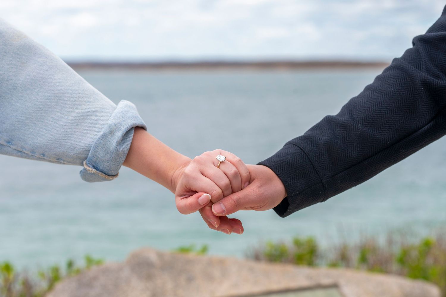 Close-up of two hands reaching toward each other against a blurred coastal background.