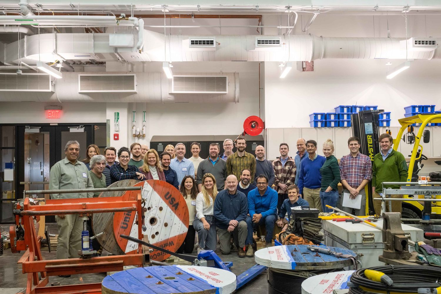 Large group of professionals posing together in an industrial workspace with equipment and tools.