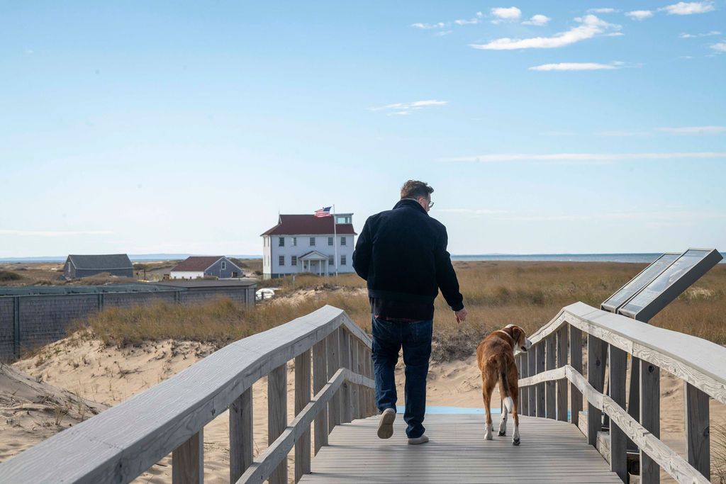 A wooden boardwalk path leads through coastal dunes under a bright blue sky.