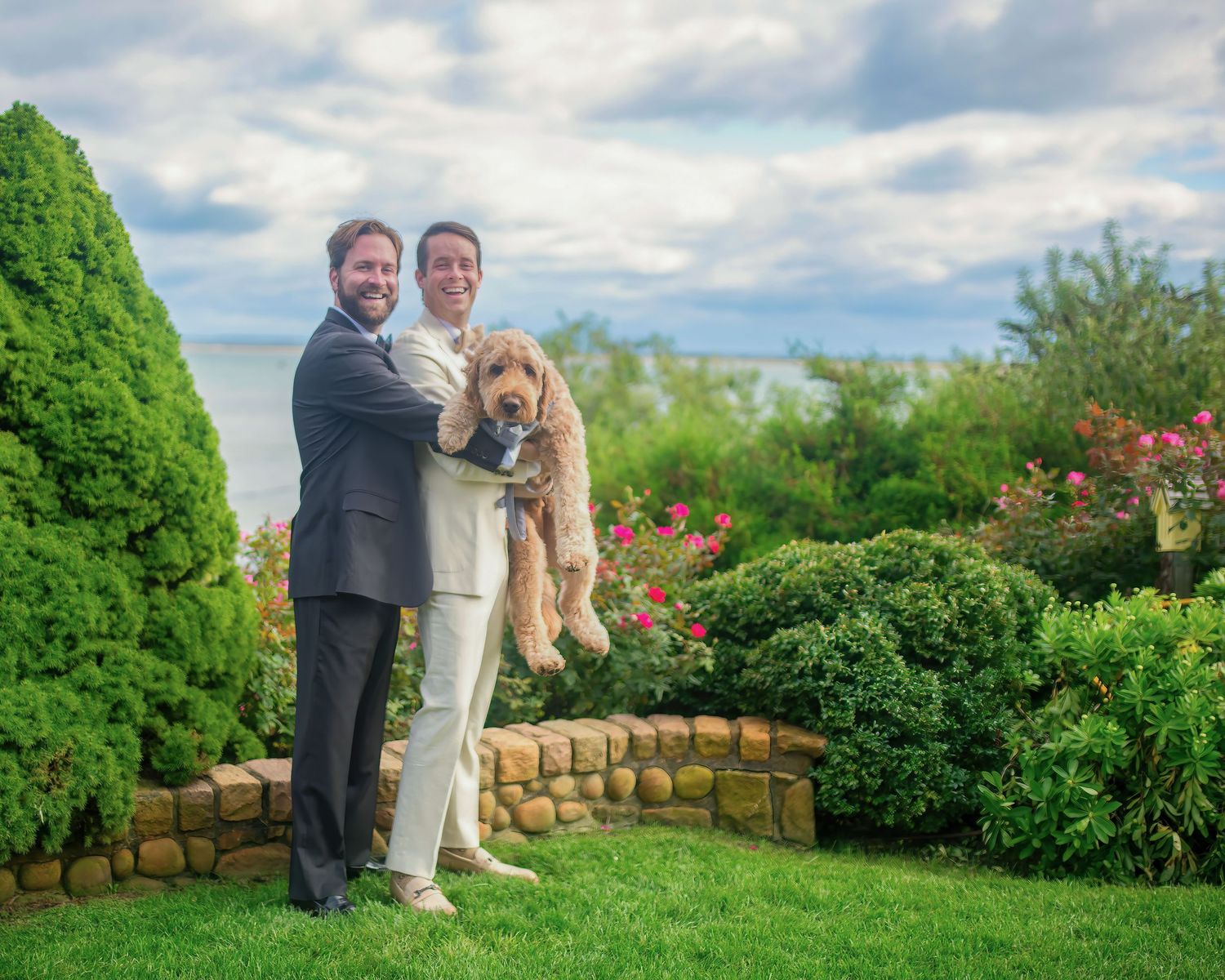 A couple poses in a lush garden setting with green hedges and blooming flowers.