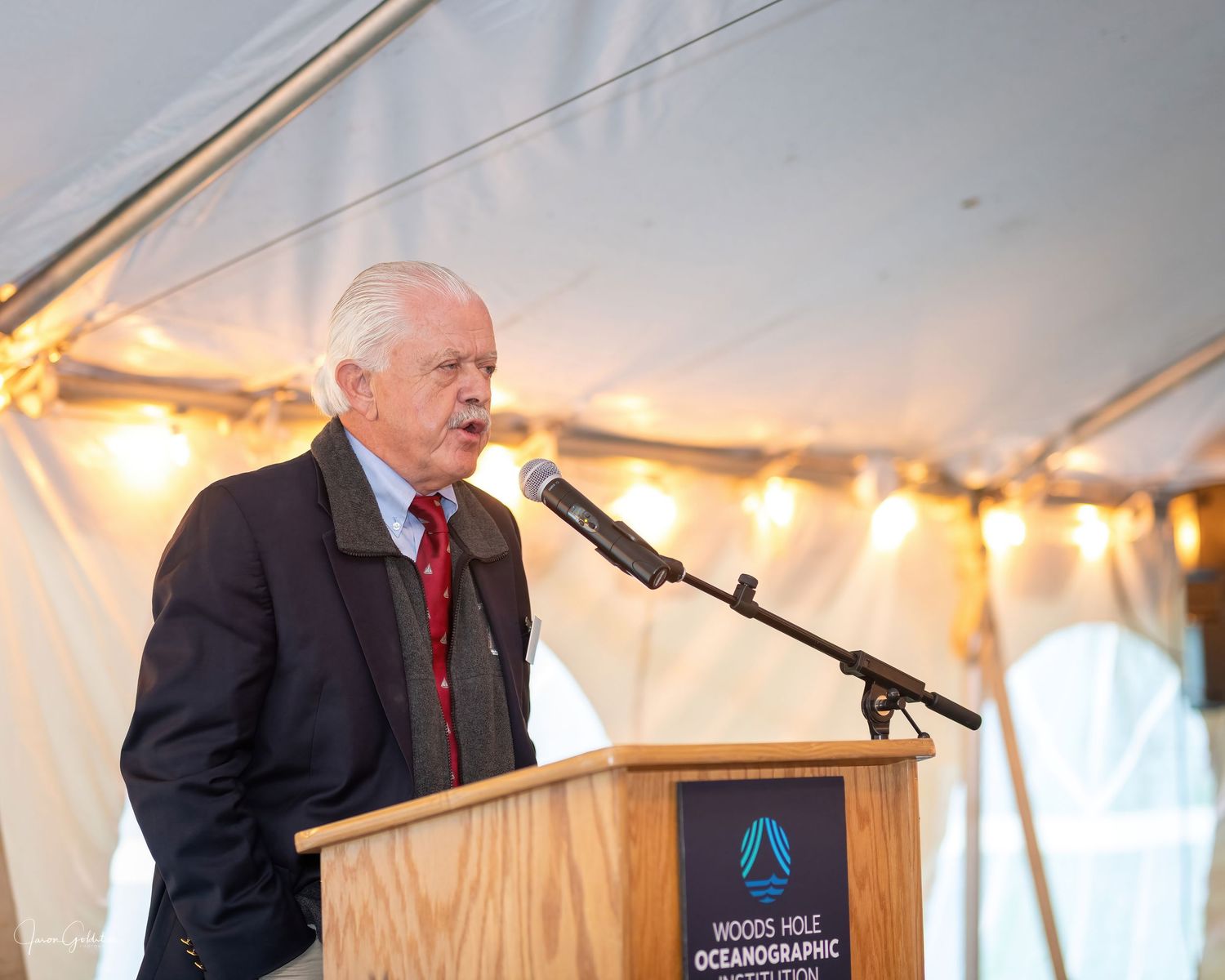 Speaker presenting at podium with Woods Hole Oceanographic Institution logo during formal event.