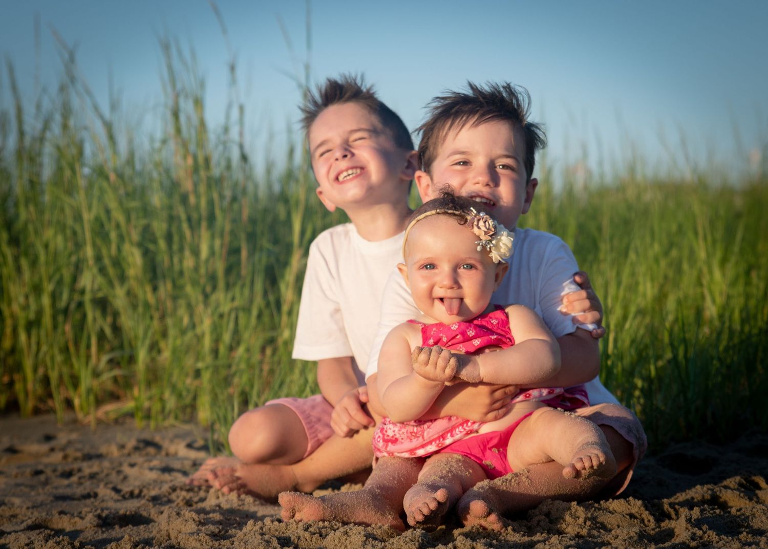 Happy group lying on sandy beach with tall grass during golden hour photography session.