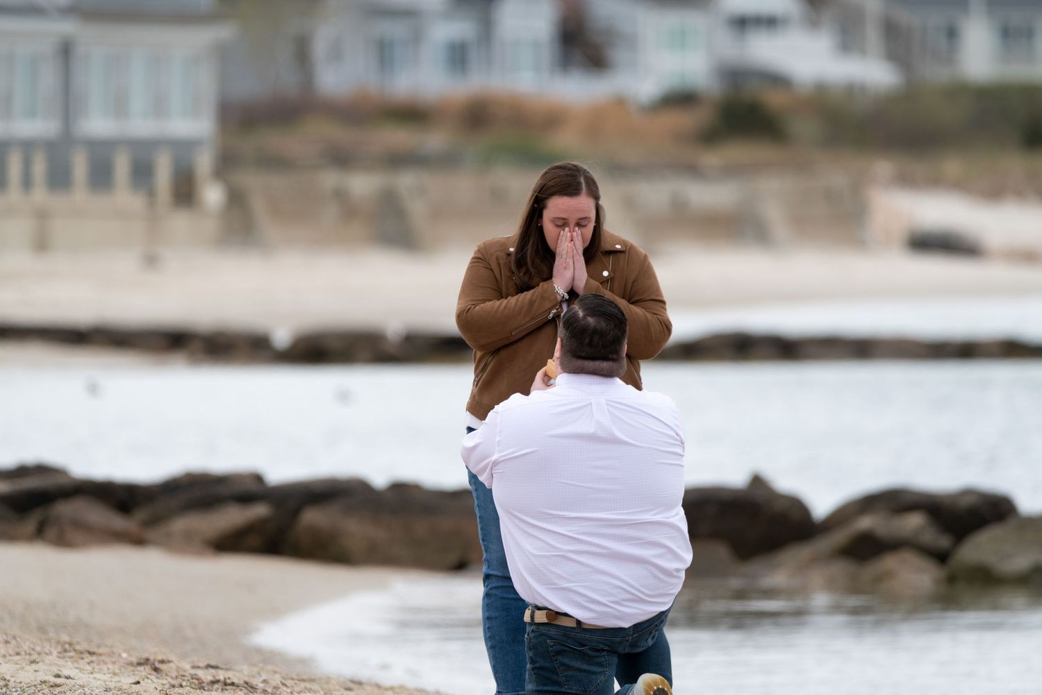 Emotional beach proposal moment captured with rocky coastline in background.