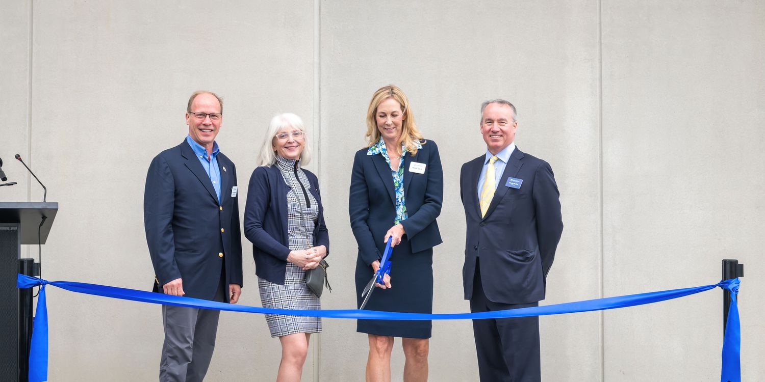 Four people stand together at a formal ribbon cutting event with blue velvet ropes.