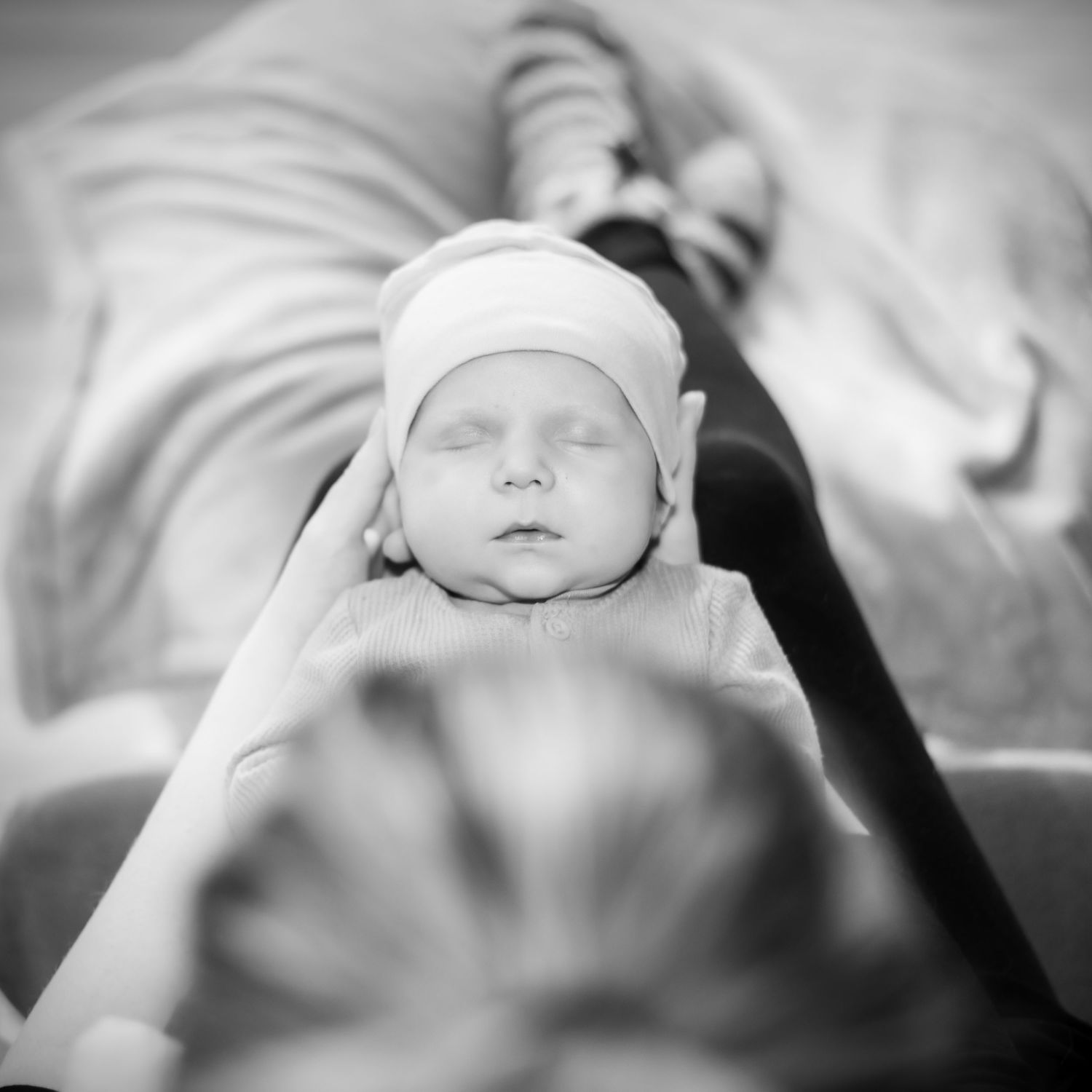 Black and white portrait of sleeping newborn wearing small cap.