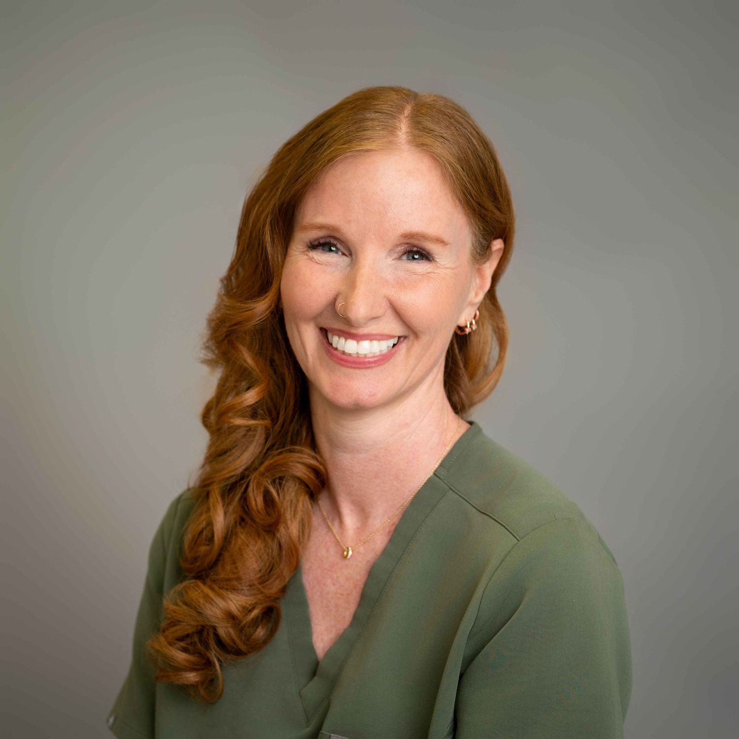 Smiling woman with red wavy hair wearing a green blouse poses for a professional headshot photo.