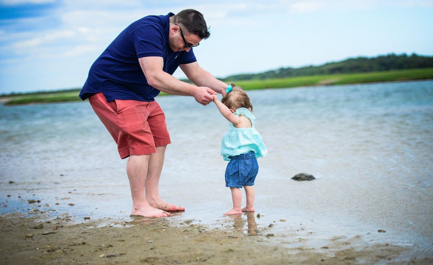 Parent and toddler explore the sandy beach together at low tide during a summer day.
