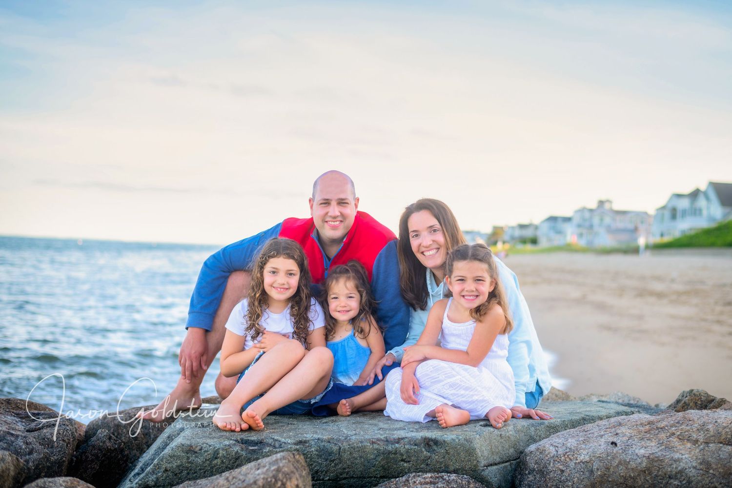 Family relaxing together on beach rocks during sunset photo session.