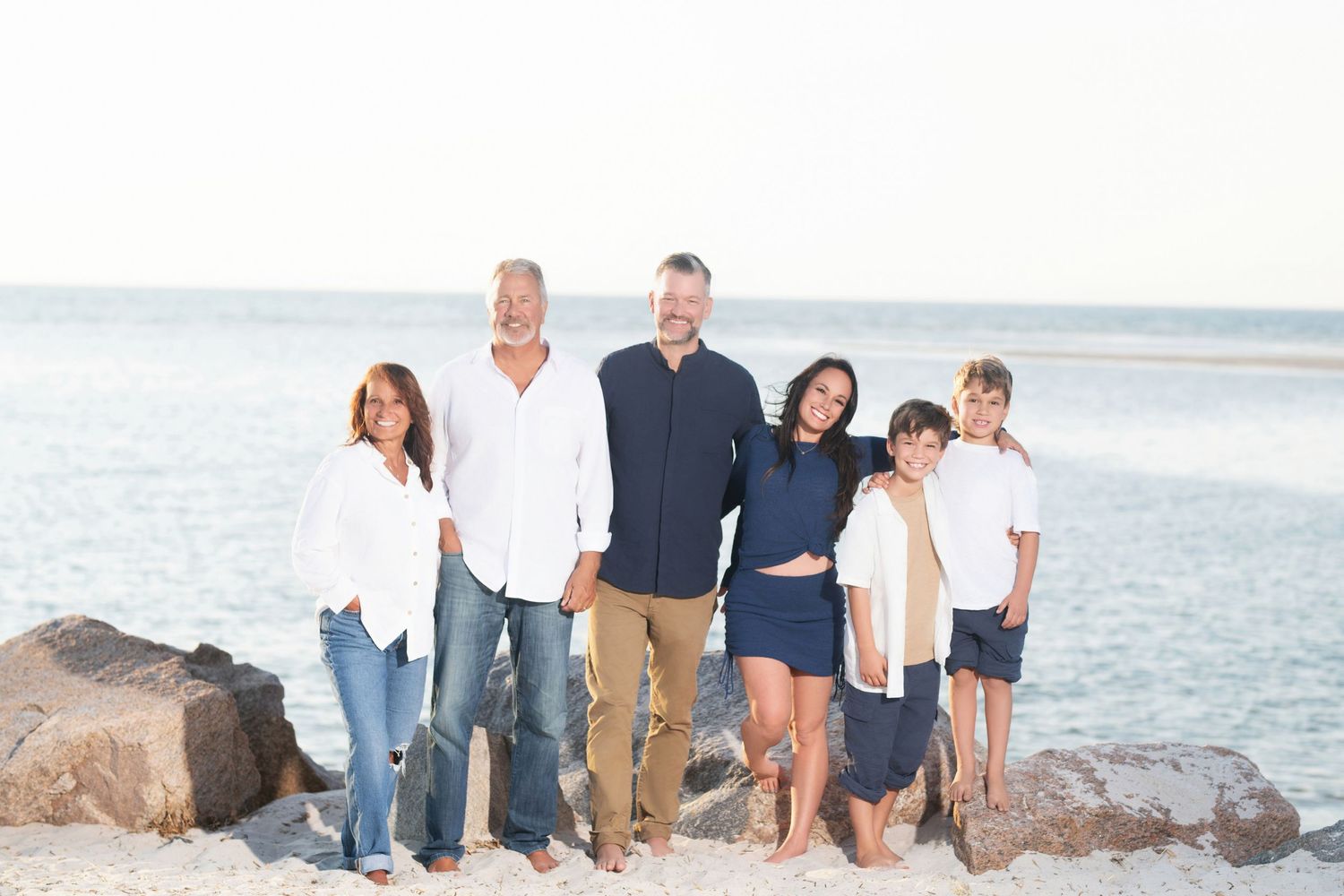 A group poses together on a beach at sunset with rocks and ocean waves in the background.