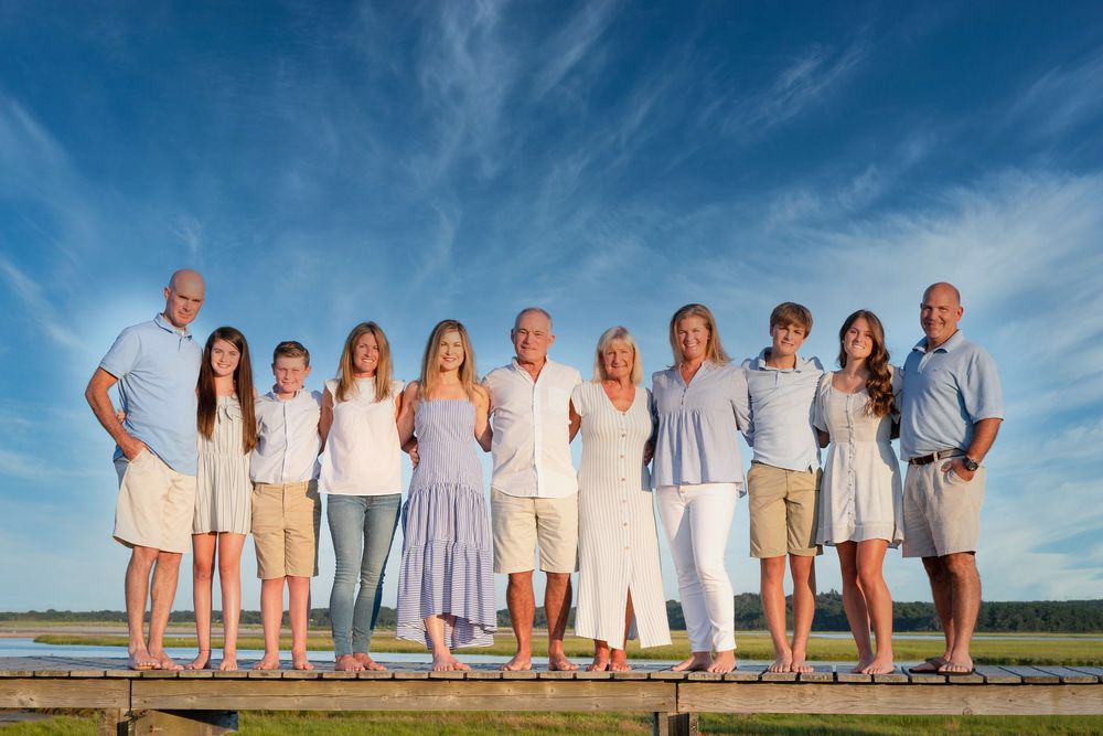 Large multigenerational family posing together on a wooden dock outdoors under a bright blue sky.