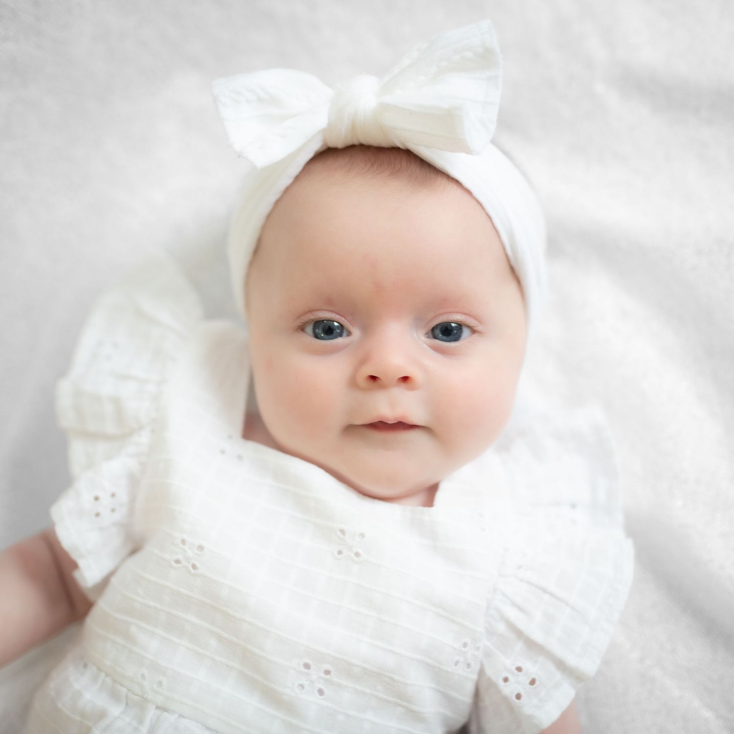 Baby wearing white bonnet and eyelet dress against white background.
