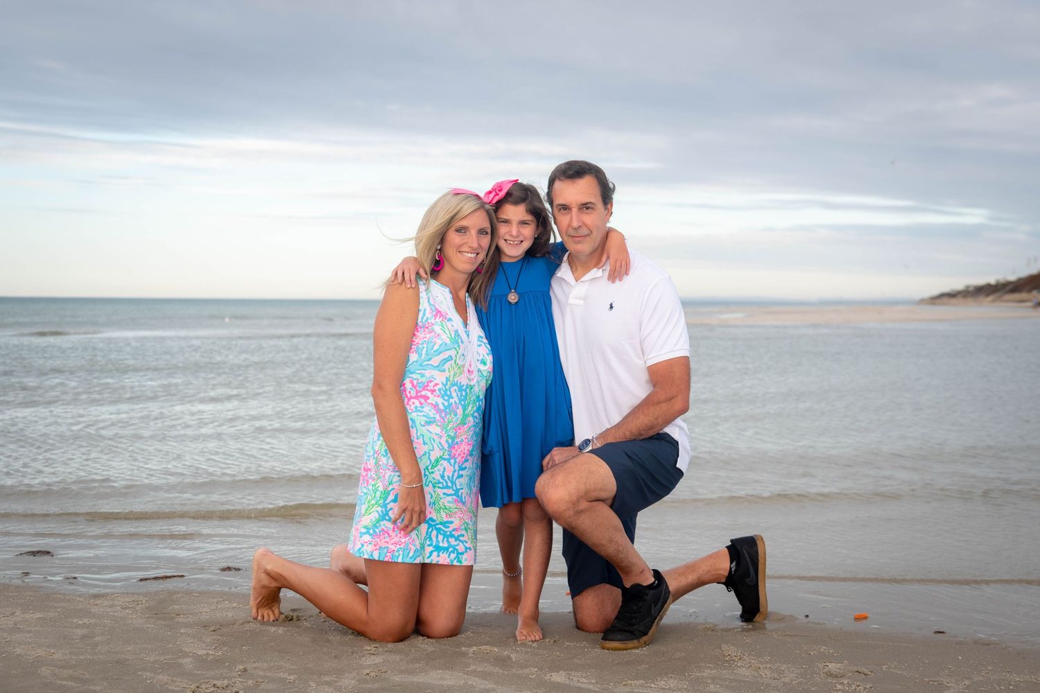 Family posing together on sandy beach with ocean backdrop.