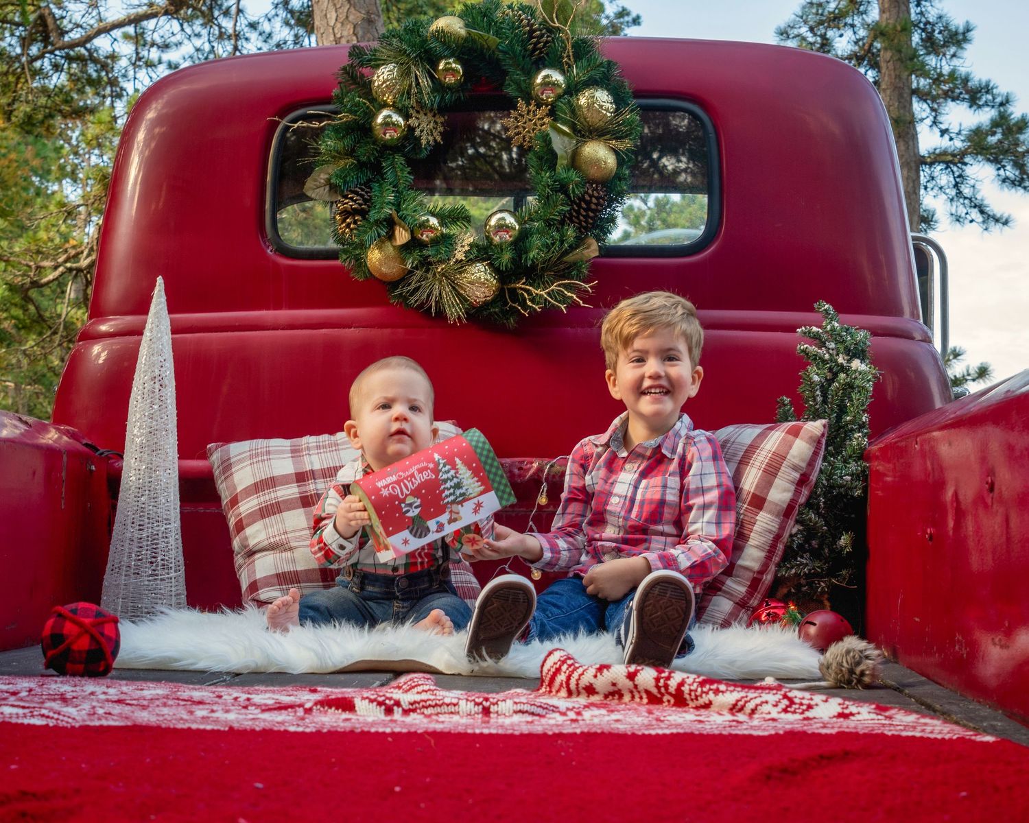 Red vintage truck decorated with Christmas wreath and holiday decor in outdoor setting.