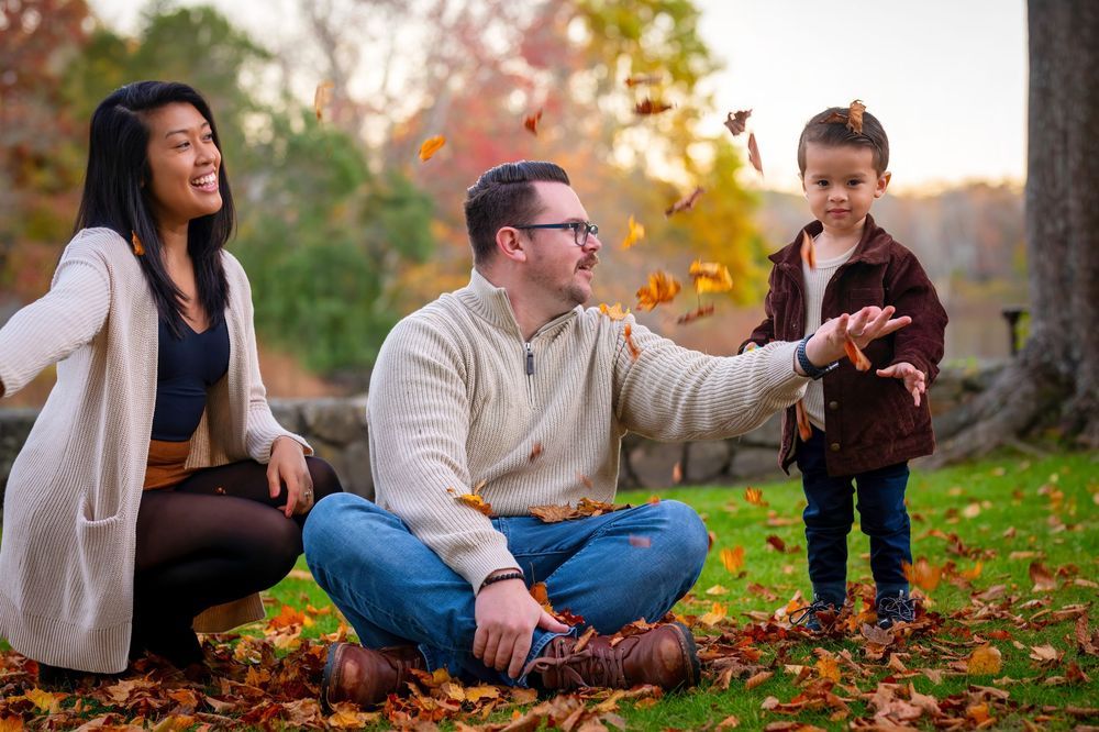 A couple sits together on autumn leaves during an outdoor photo session in a park.