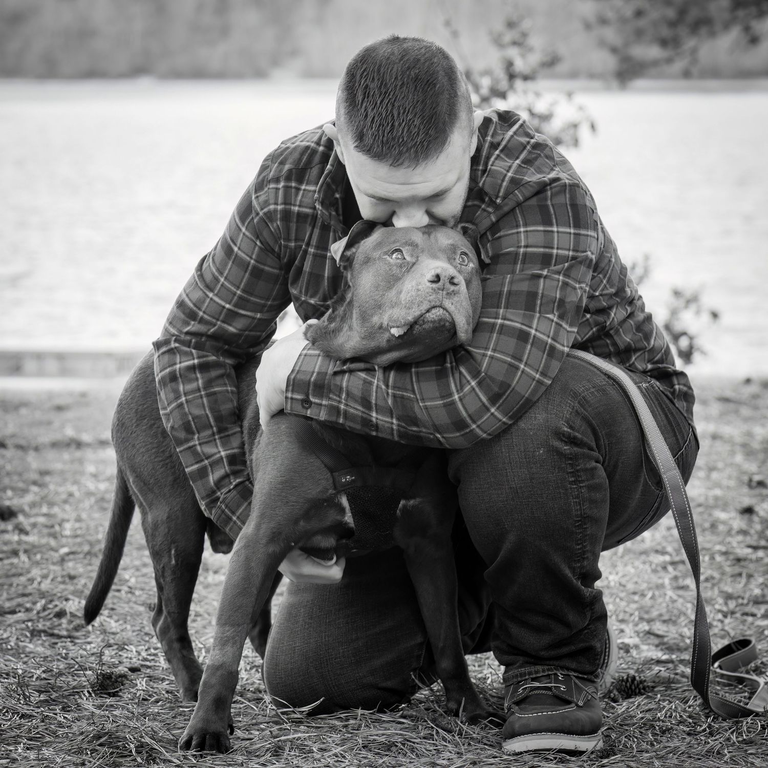 Black and white photo of a tender moment between a person in plaid and their dog.