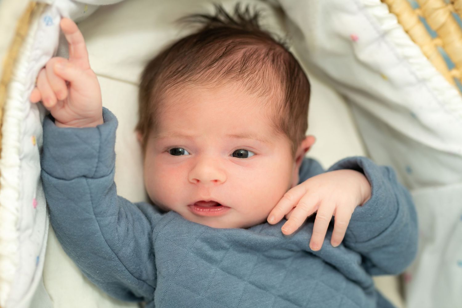 Baby wearing blue outfit lying in cozy white bedding.