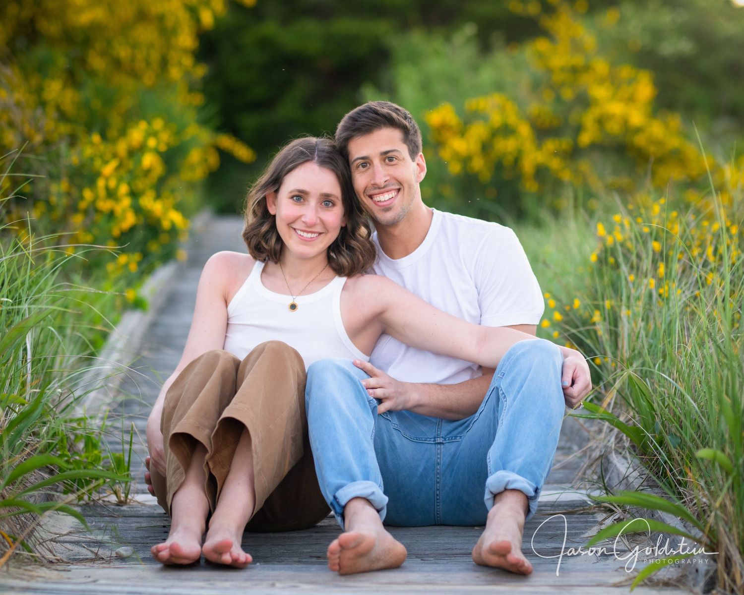 Romantic couple sitting together among blooming yellow wildflowers by the coast.