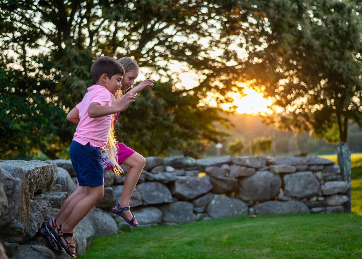 Children playing and climbing on stone walls during a summer evening outdoors.