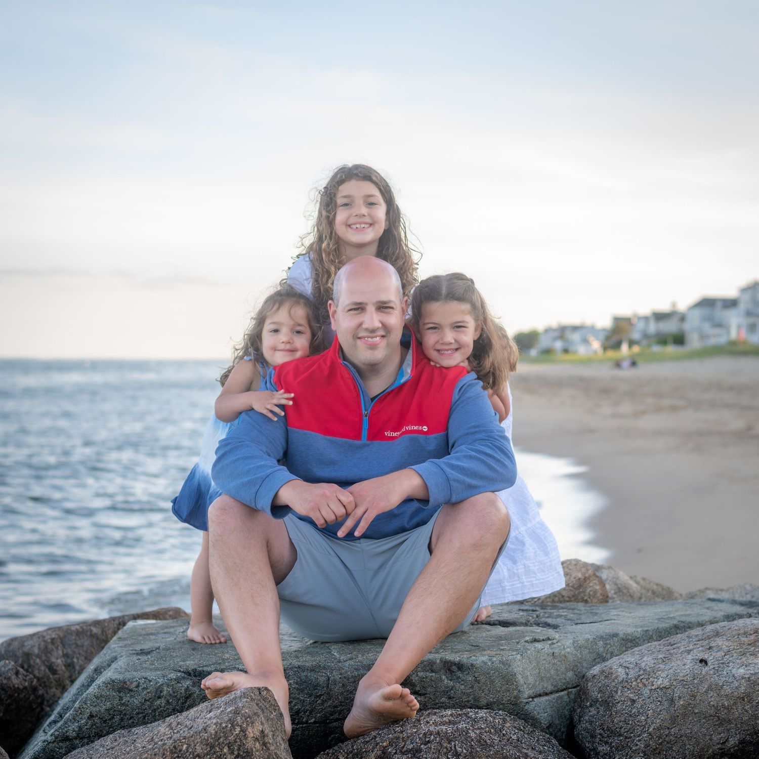 Family relaxing together on rocky beach during sunset.