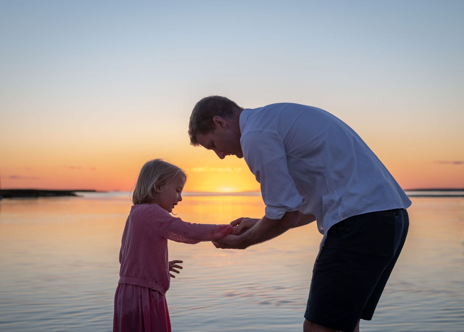 Family enjoying a beautiful sunset together on a beach with calm waters in the background.