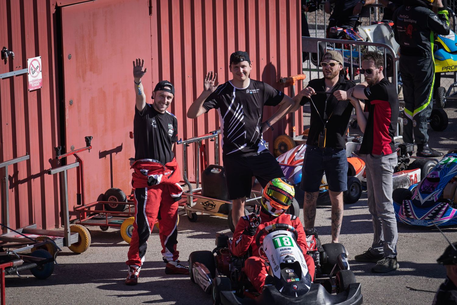 Spectators cheer on go-kart racers from behind red barriers at outdoor racing event.