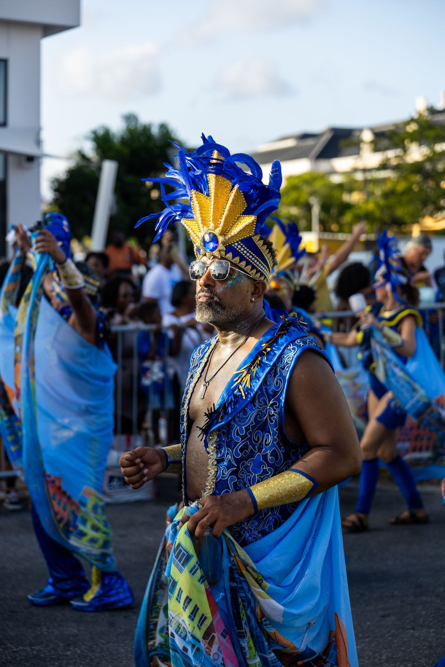 Carnival dancers in vibrant blue and gold costumes perform at an outdoor festival celebration.