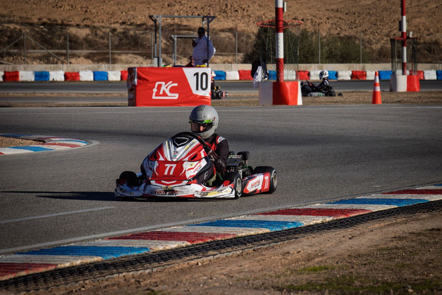 Go-kart racer navigates a tight turn on a race track with red and blue curbing.