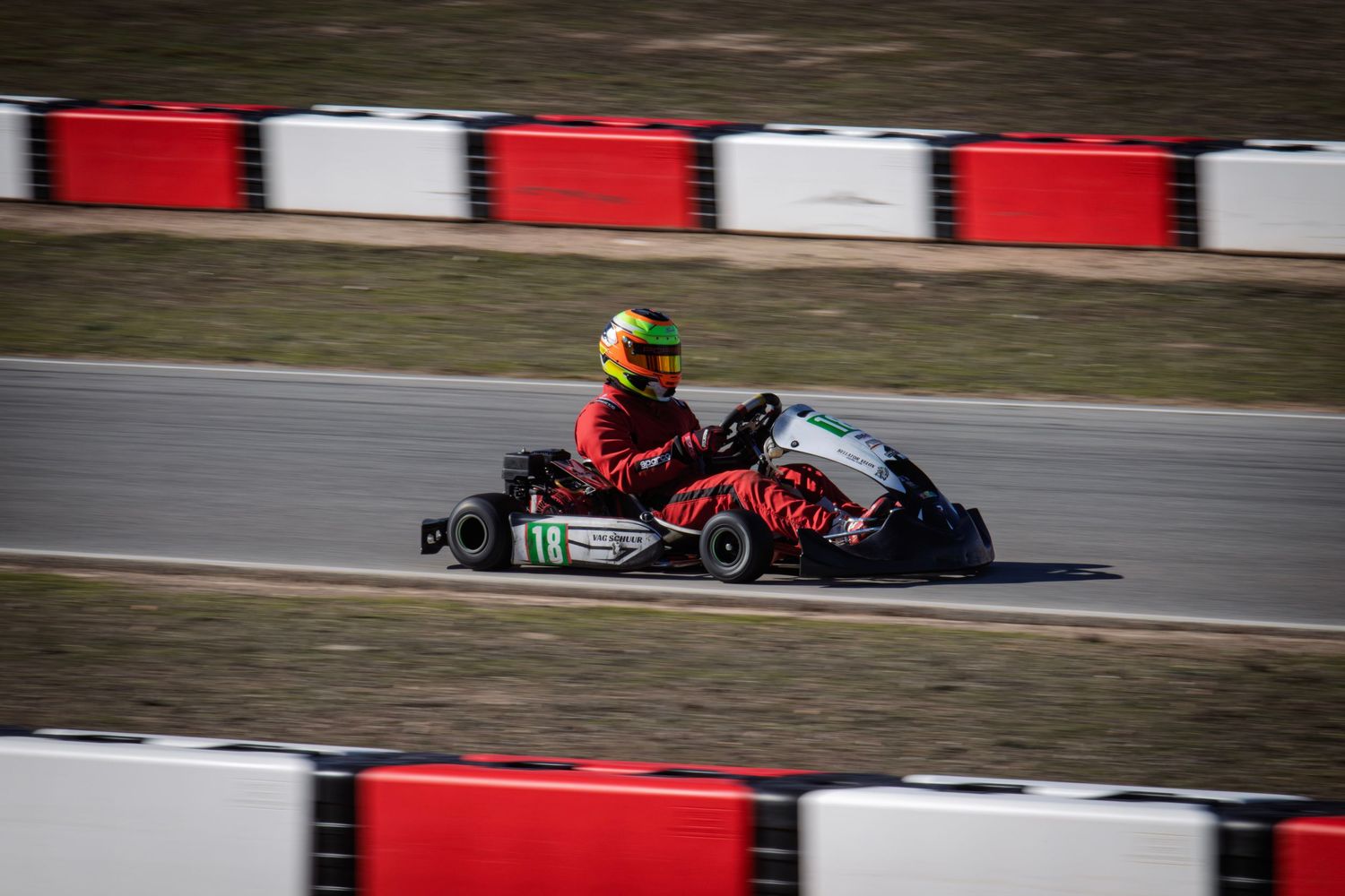 Go-karts competing for position on a race track with red and white safety barriers.