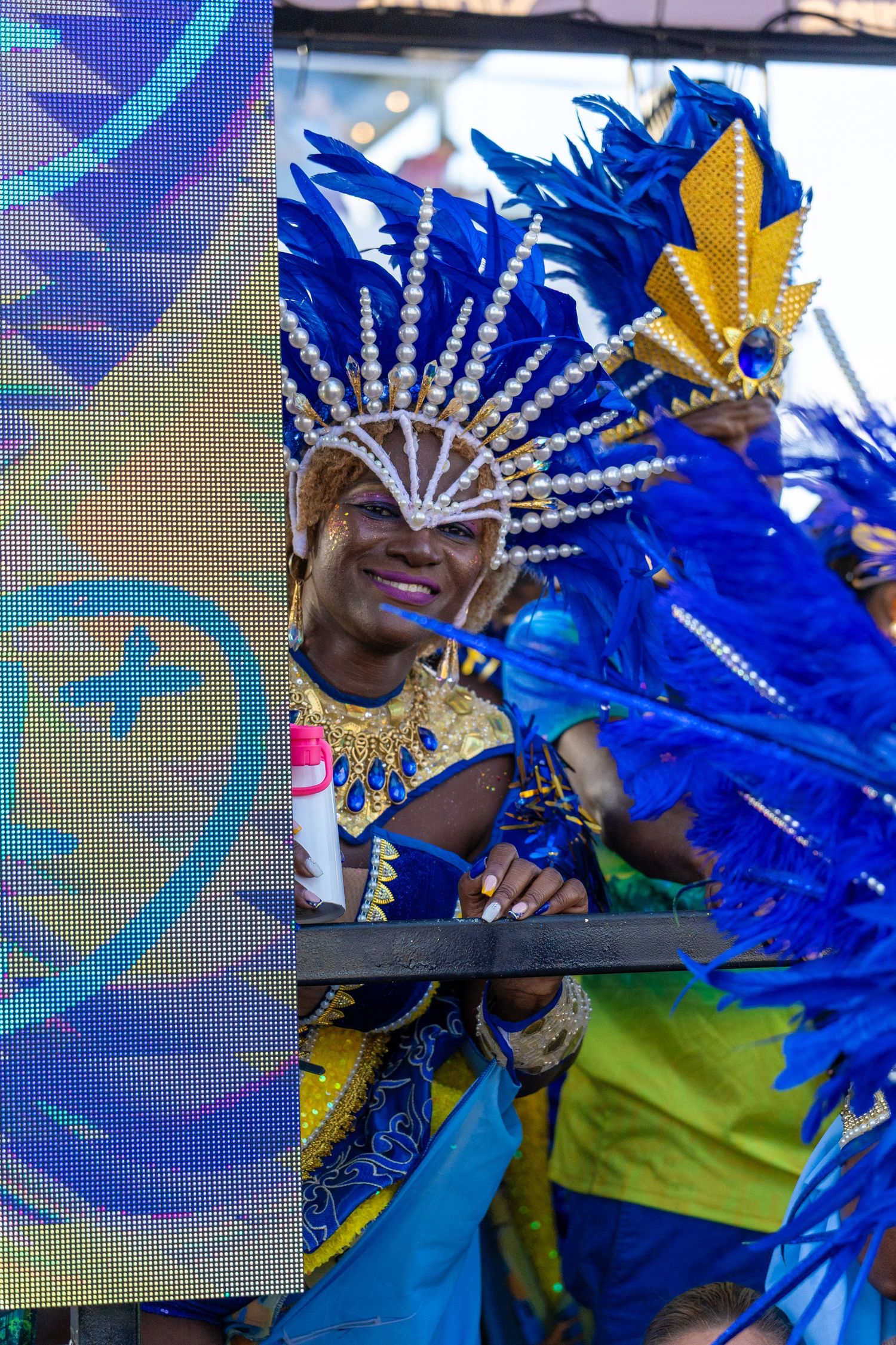 Performer wearing blue feathered headdress and gold accents dances during carnival celebration.
