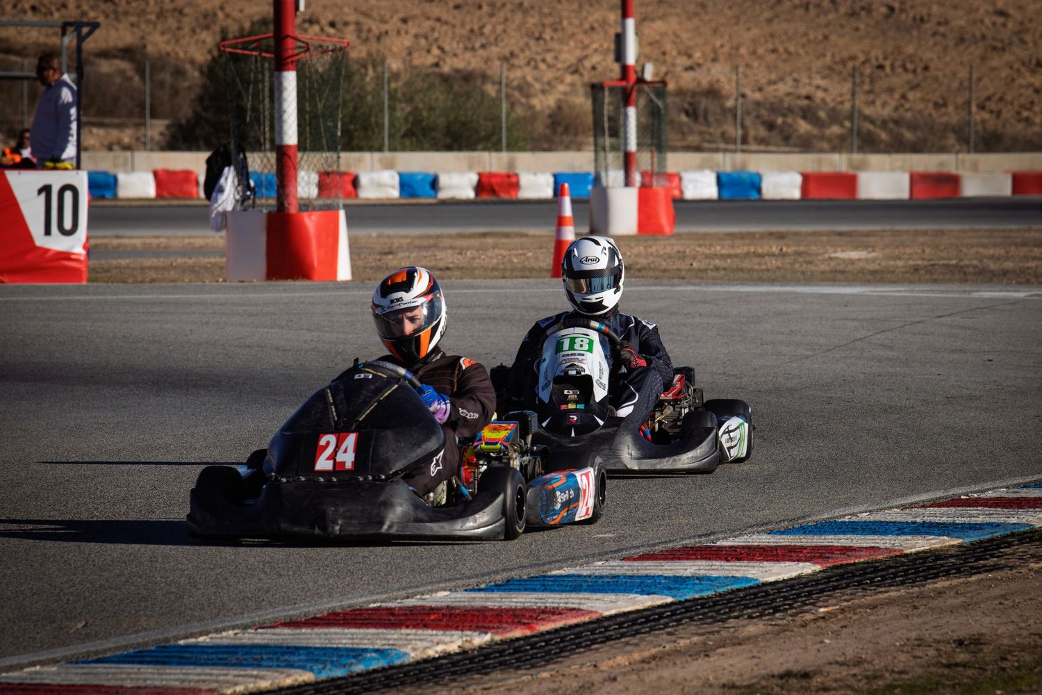 Two go-karts compete side by side through a challenging race track corner.