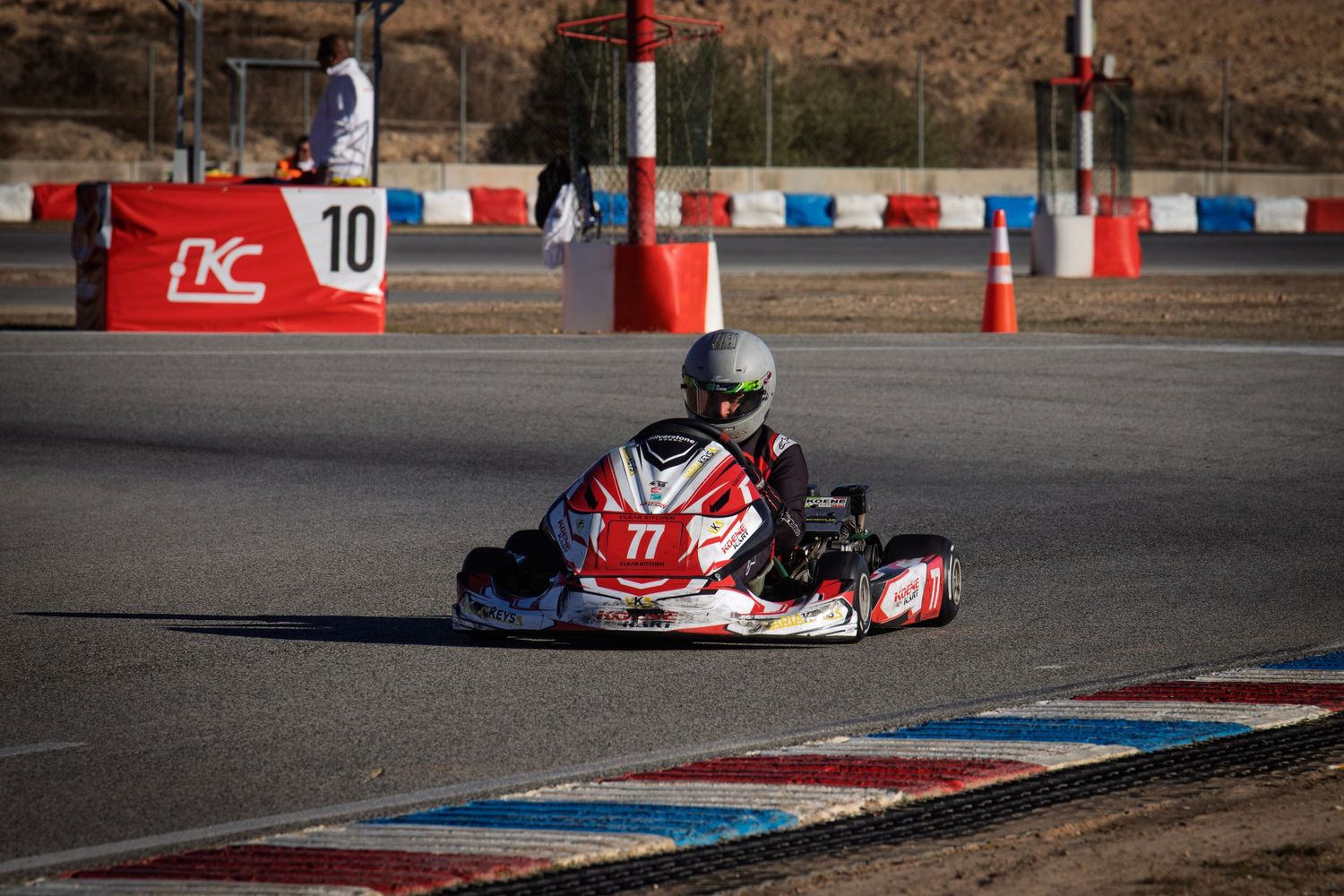 Red and white go-kart takes a racing line through a corner with red barriers.