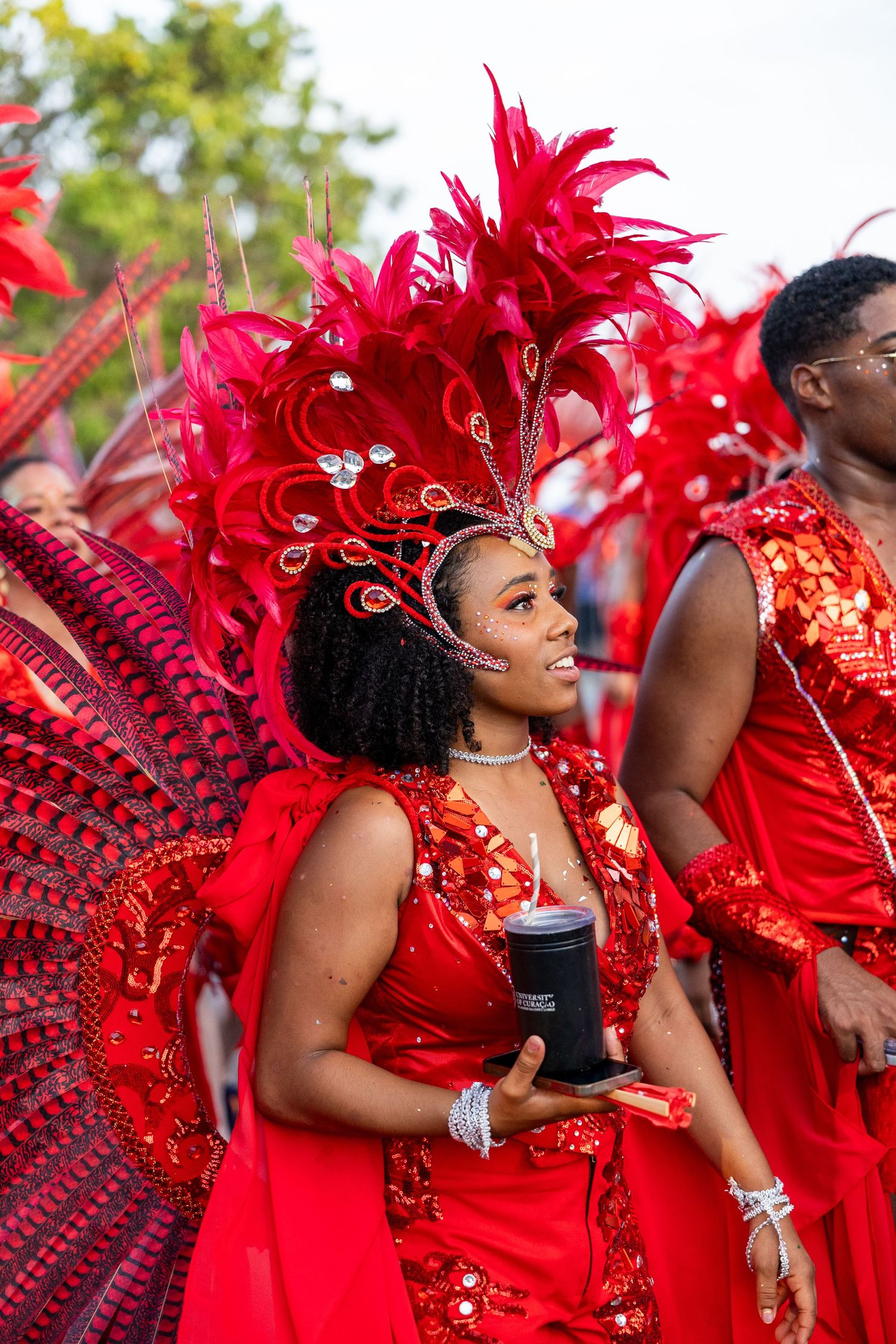 Dancers in vibrant red costumes with feathered headdresses perform at a carnival celebration.