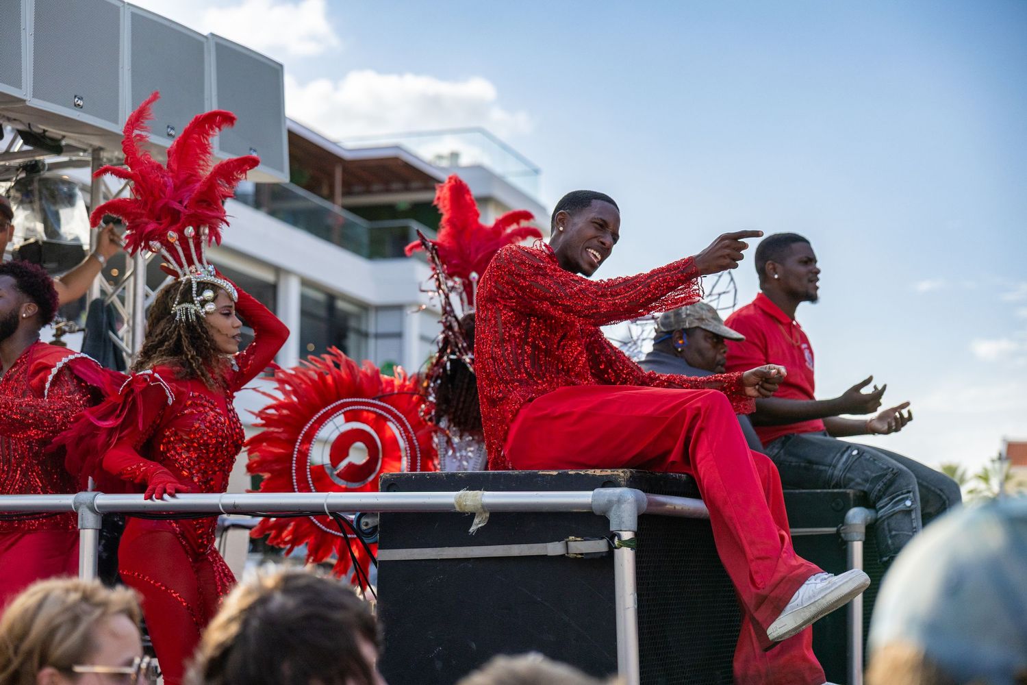 Performers in red costumes dance and gesture on a raised platform during an outdoor event.