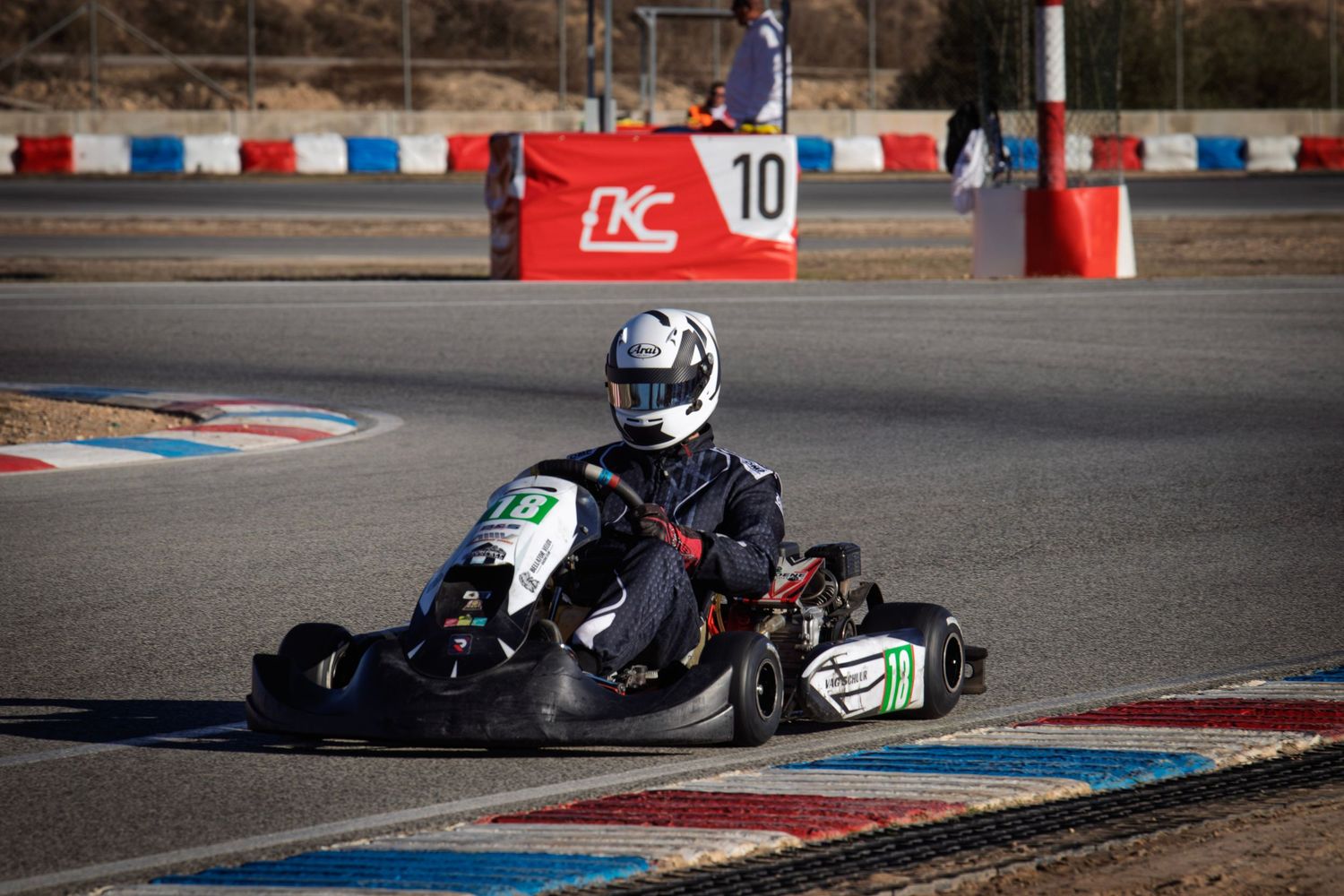 Go-kart in black and green livery races through a technical corner section.