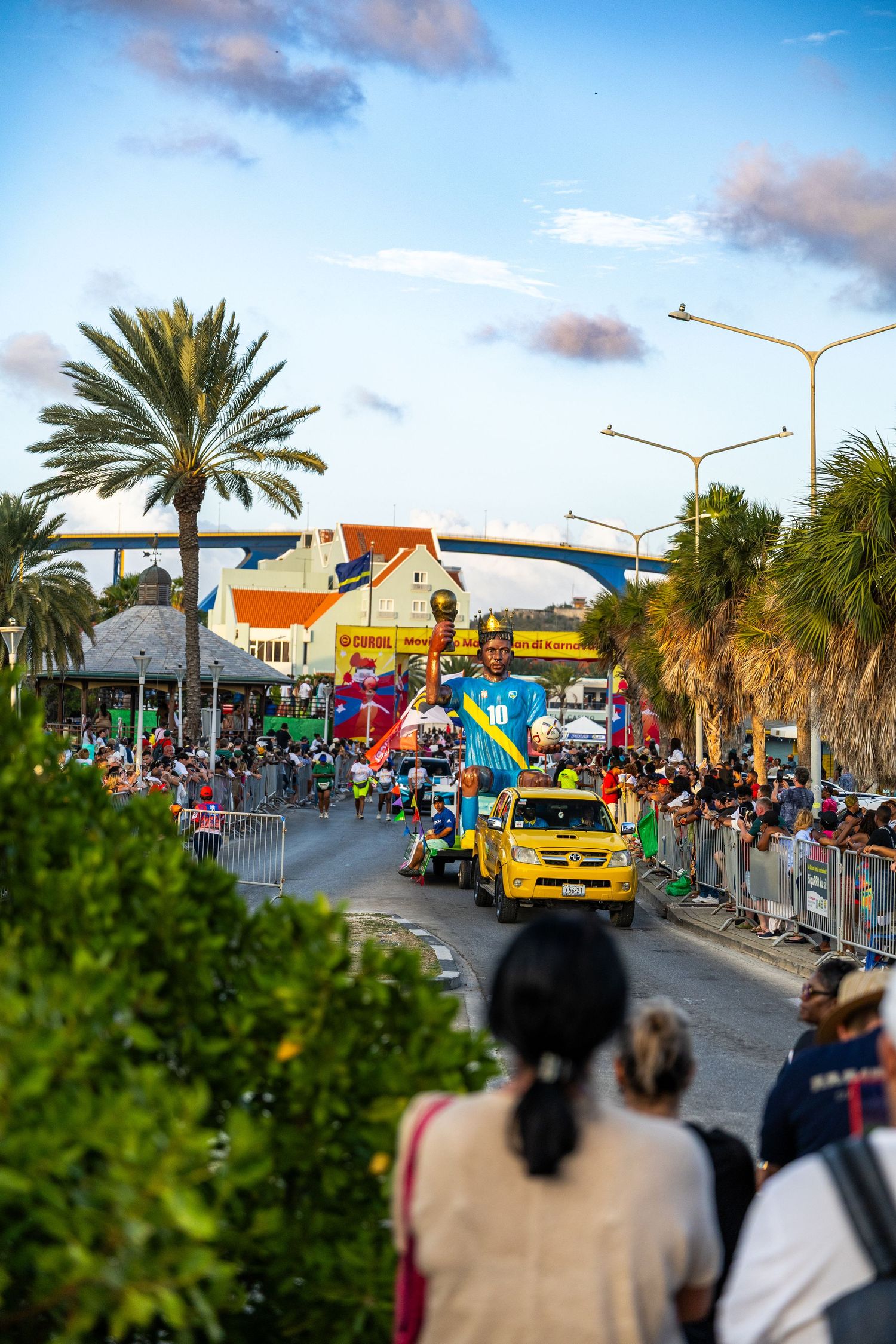Palm trees line a crowded street festival route with spectators watching parade.
