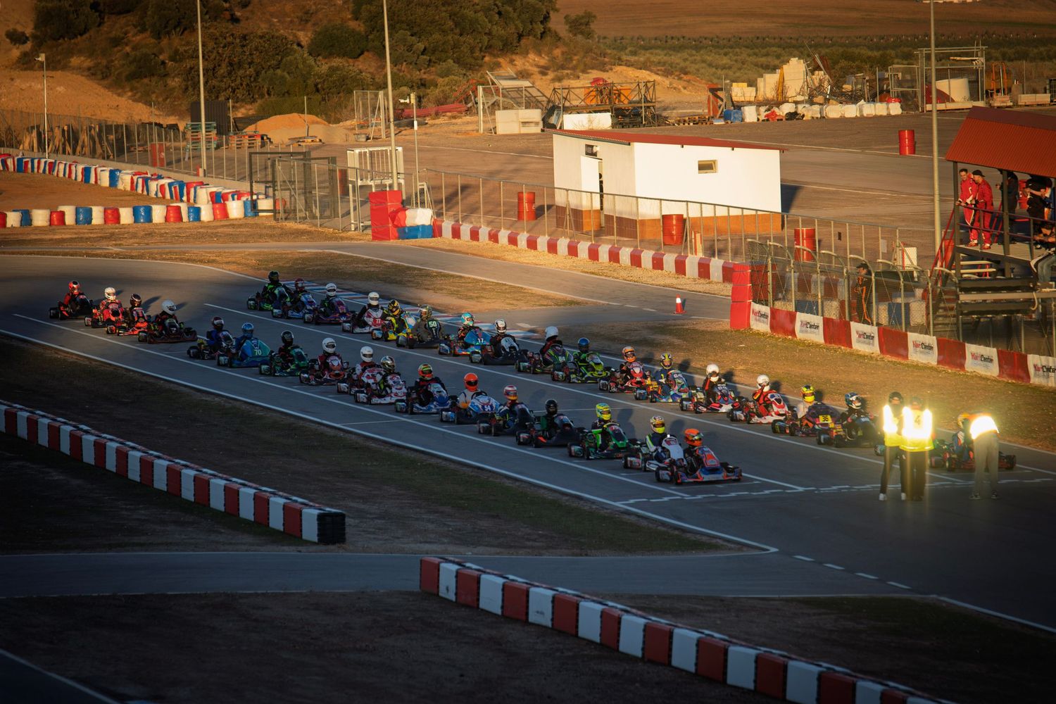 Go-karts racing at dusk on illuminated track with red and white barriers.