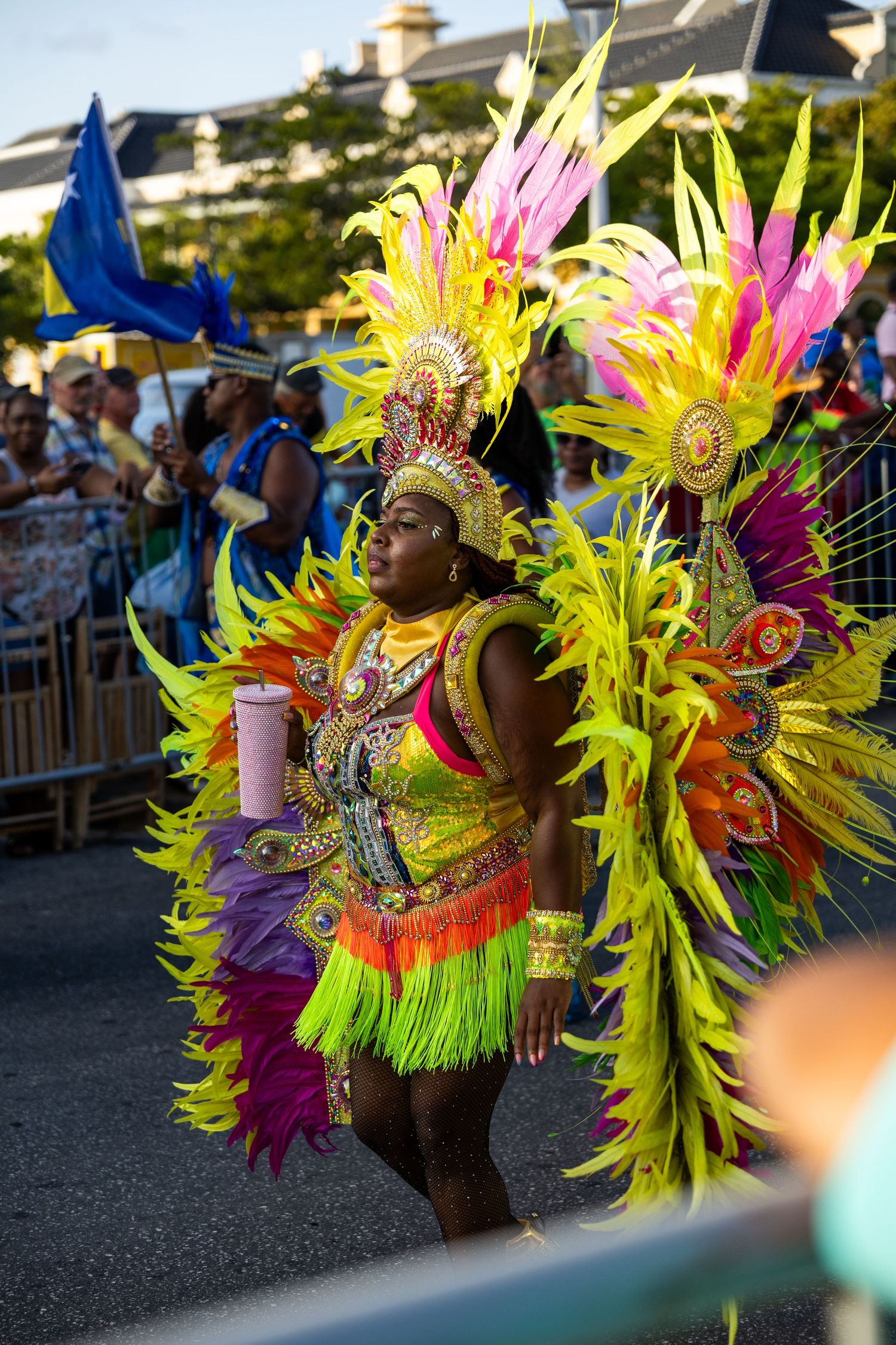 Carnival dancer in vibrant neon feathered costume performs during street parade.