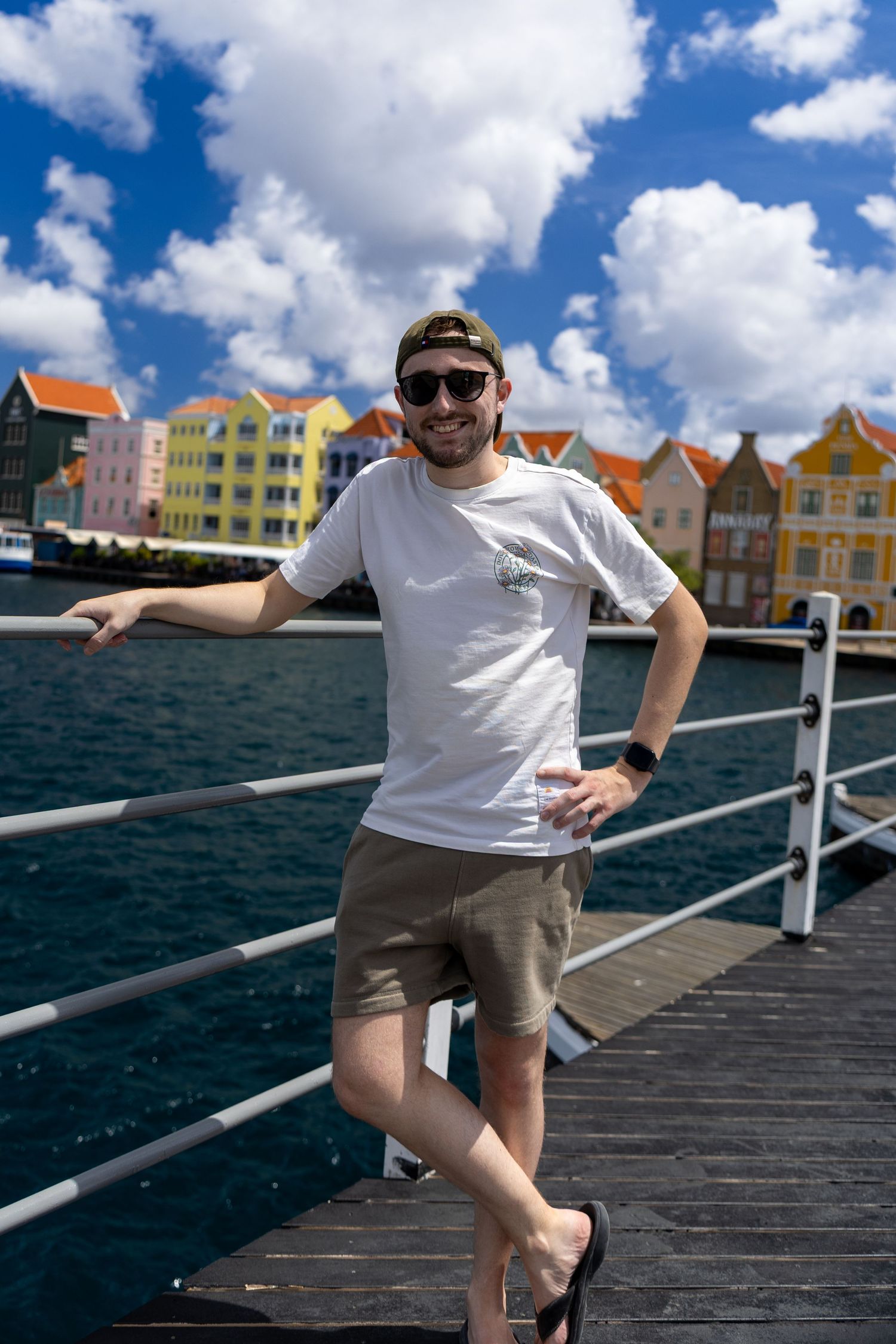 Tourist poses on waterfront boardwalk with colorful historic buildings of Curacao in background.